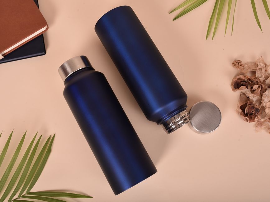 Stylish blue insulated sport bottles accompanied by notebooks and natural leaves for a modern still life composition.